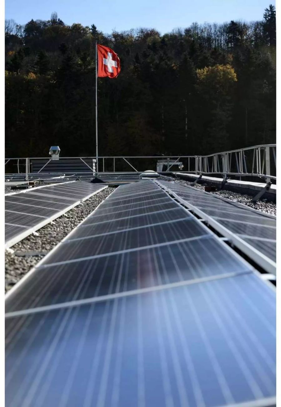 Solarpanels auf einer Solarfarm mit einer Schweiter Fahne im Hintergrund - Keystone