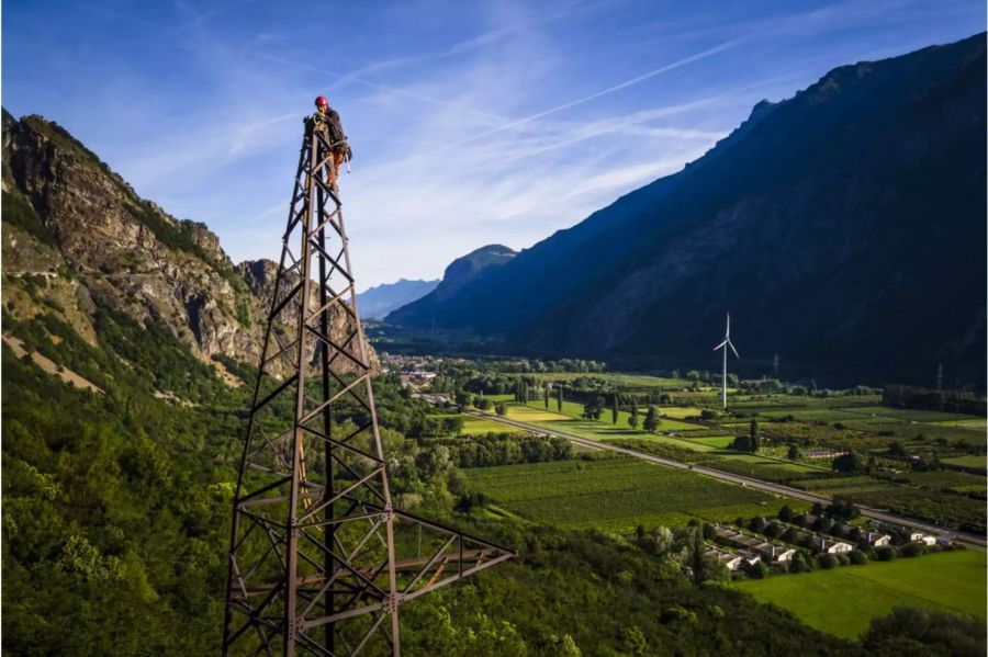 Mann auf der Spitze eines Strommastes und im Hintergrund eine Windturbine - Keystone