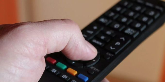 Eine Person hält eine Fernbedienung eines Fernsehens in der Hand. (Symbolbild) Daumen auf einer TV-Bedienung.