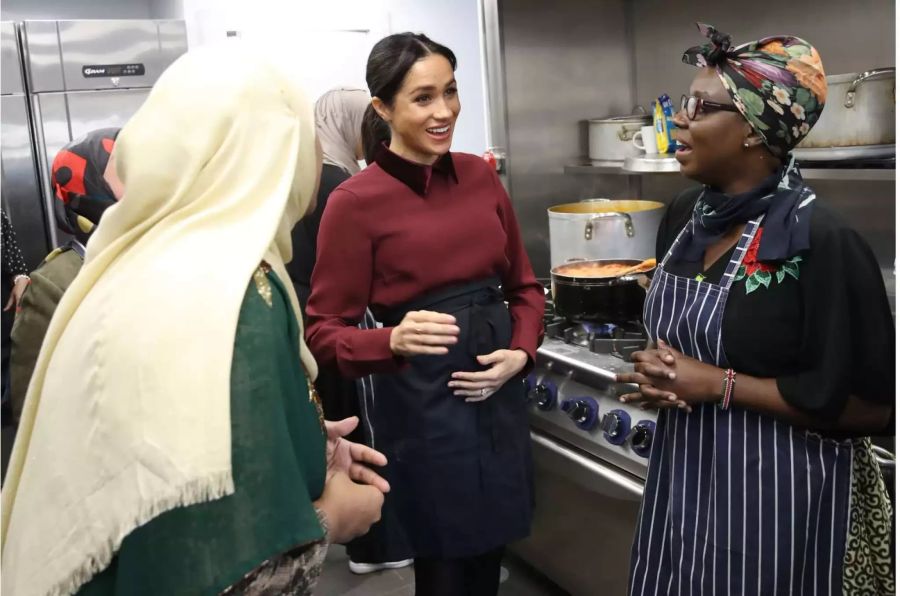 Meghan spricht mit Frauen während ihres Besuchs in der «Hubb» Gemeindeküche und hält sich glücklich den Bauch.