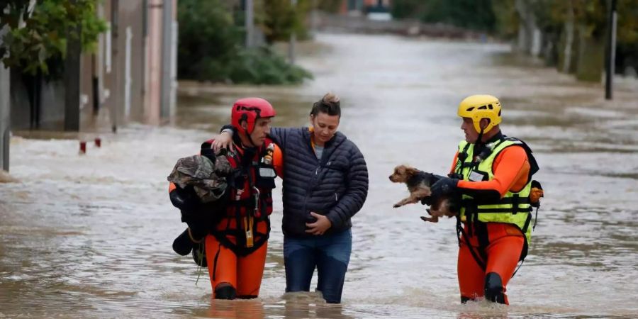 Französische Feuerwehrleute helfen einer Frau und einem Hund durch eine überflutete Strasse.