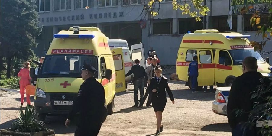 Krankenwagen, Rettungskräfte und Polizisten sind nach einer Explosion in der Mensa der Berufsschule auf der Halbinsel Krim vor dem Gebäude zu sehen.