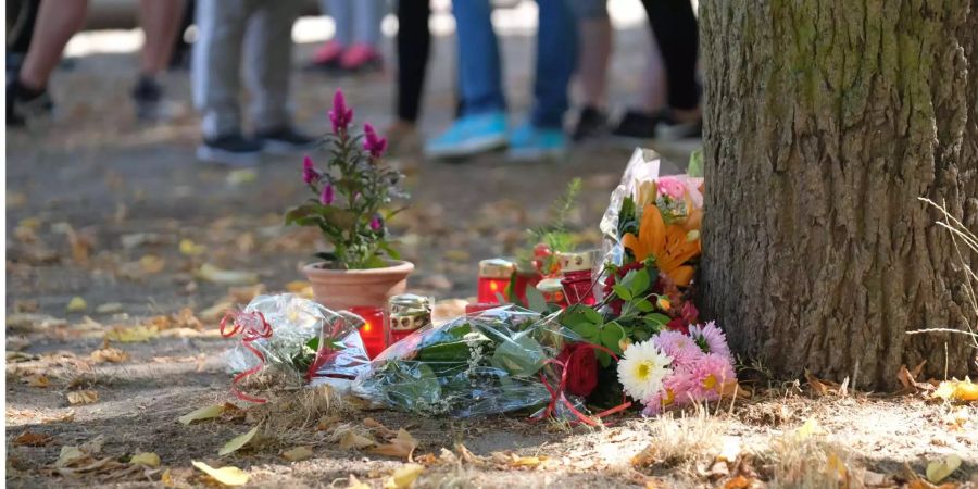 Blumen und Kerzen stehen an einem Baum auf einem Spielplatz.