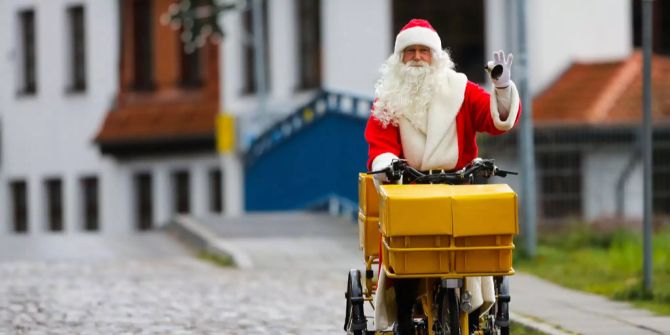 Ein Mann in Weihnachtsmannverkleidung fährt auf einem Post-Fahrrad.