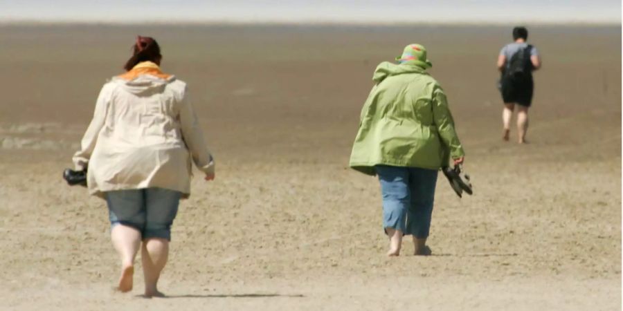 Drei Frauen laufen barfuss am Strand.