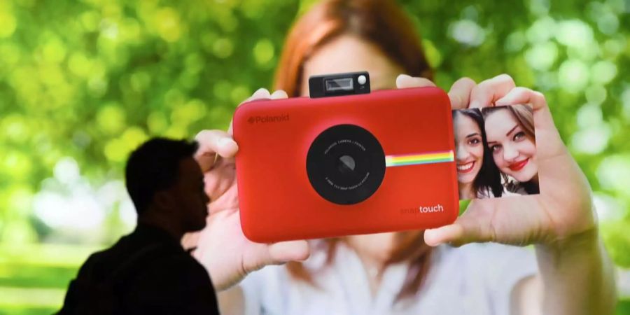 Eine Frau zeigt eine Sofortbildkamera von Polaroid.