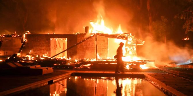 Ein Feuerwehrmann geht ab einem brennenden Haus vorbei.