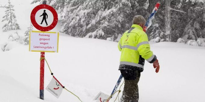 Ein Mitarbeiter eines Schneegebiets sperrt wegen der Lawinengefahr den Fussweg.
