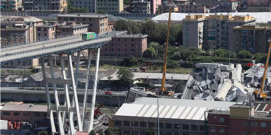 Mit Baggern und Kränen werden Trümmerteile einer teilweise eingestürzten Brücke weggeräumt, während auf der Brücke ein LKW immer noch an der Bruchkante steht.