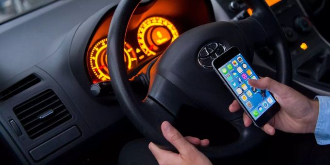 Ein Autofahrer blickt während der Fahrt aufs Handy. Auto Handy