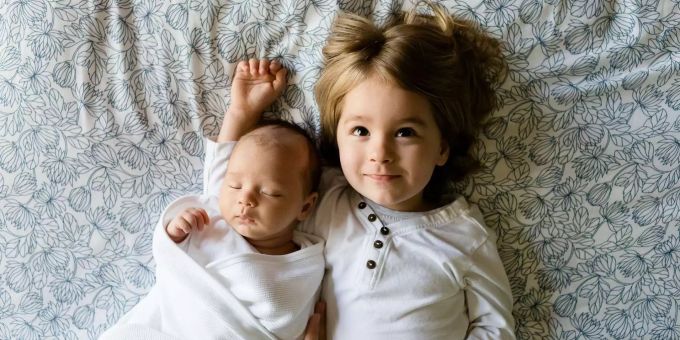 Zwei Kinder liegen auf einer Decke. Baby Schwester