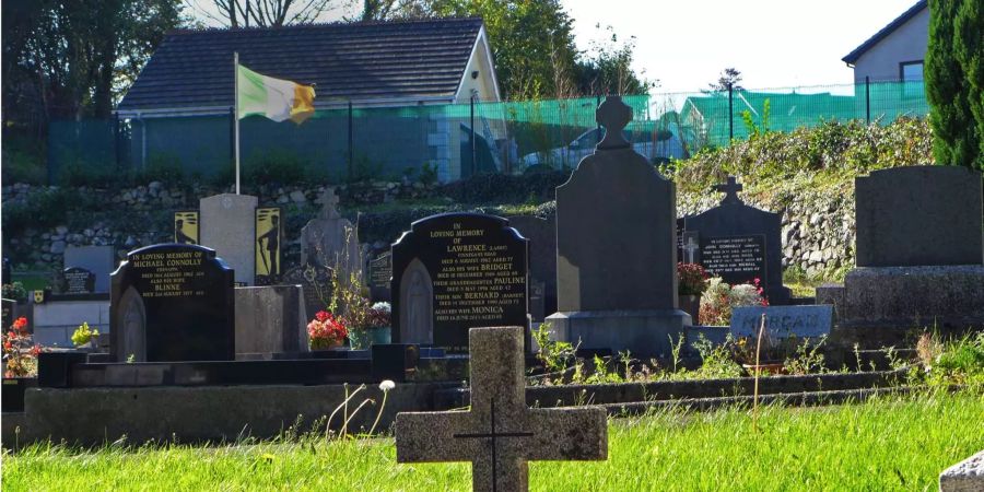 Eine irische Flagge weht über den Gräbern auf einem Friedhof in Carrickcarnan, direkt neben der Kirche Jonesborough Parish in Nordirland.