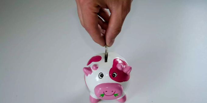 Jemand schmeisst Geld in eine pinke Sparkuh. Jemand schmeisst Geld in eine pinke Sparkuh.