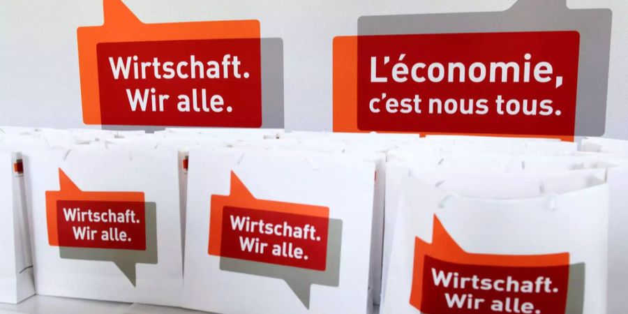 Informationstüten mit der Aufschrift «Wirtschaft. Wir alle.» stehen vor einer Wand mit demselben Schriftzug an einer Tagung der Economiesuisse in Genf.