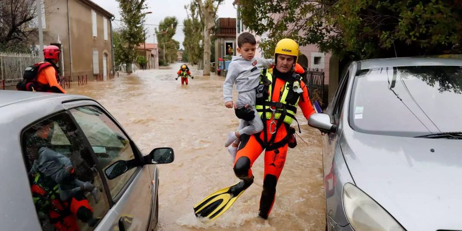 Ein französischer Feuerwehrmann trägt ein Kind durch eine überflutete Strasse.