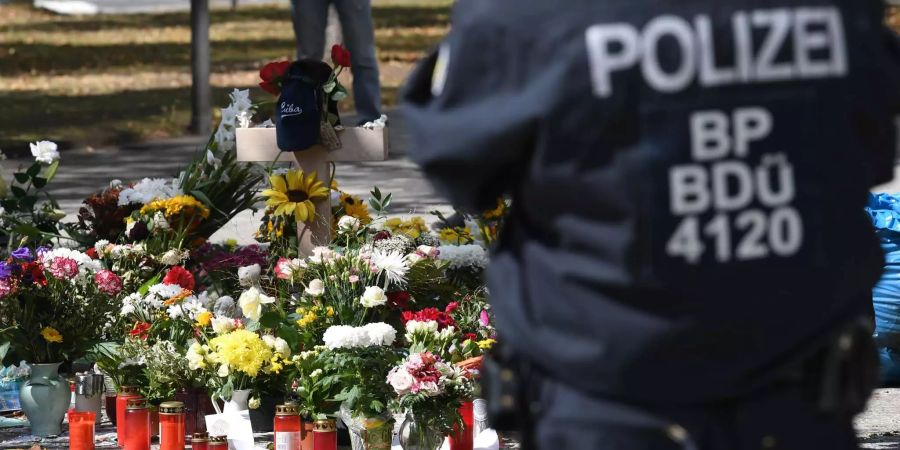 Bei einer Gedenkveranstaltung am Tatort, wo ein 35-jähriger Deutscher bei einer Messerattacke getötet wurde, steht ein Polizist neben den Blumen.