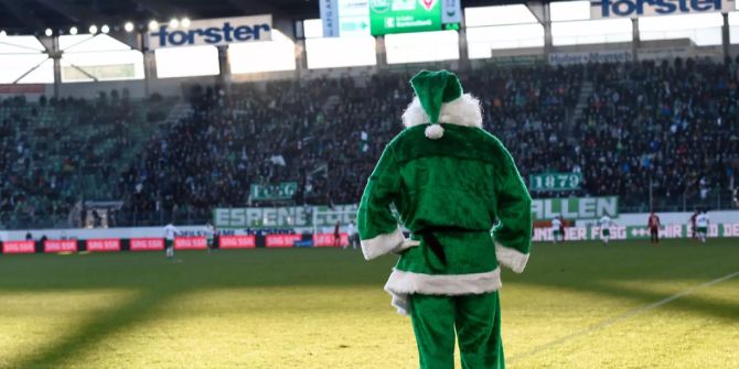 Ein grüngewandter Samichlaus verfolgt ein Fussballspiel,