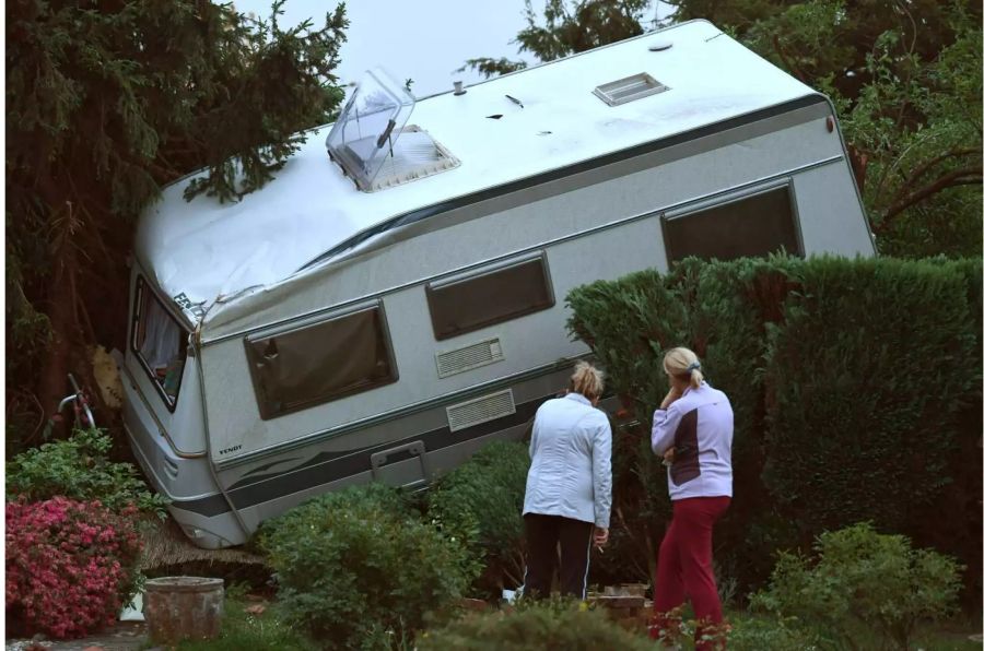 Zwei Frauen betrachten ein Wohnmobil, das nach einem Wirbelsturm in einen Garten liegt.