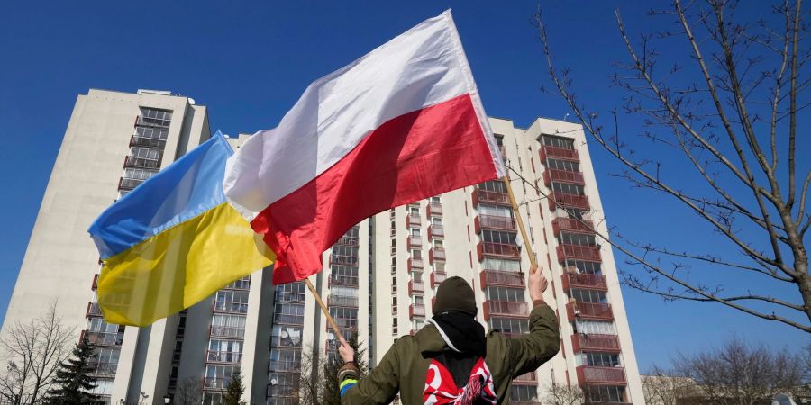 Ein Mann schwenkt während einer Demonstration in Warschau die ukrainische und die polnische Flagge vor einem Gebäude, in dem russische Diplomaten untergebracht sind.