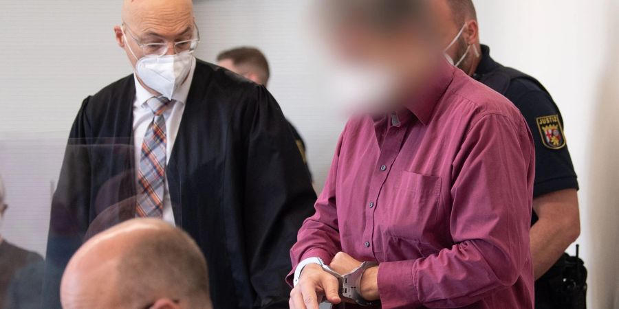 Der Angeklagte wird in Handschellen in den Gerichtssaal gebracht. Neben ihm steht sein Verteidiger Alexander Klein (l).