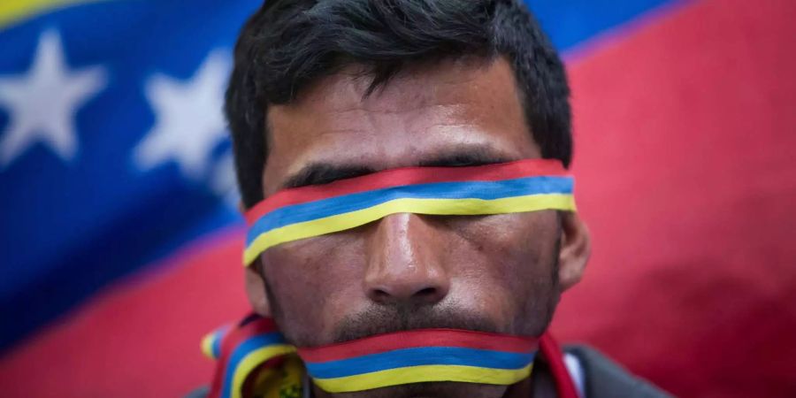 Ein Mann hat sich den Mund und die Augen mit der Flagge Venezuelas zugedeckt.