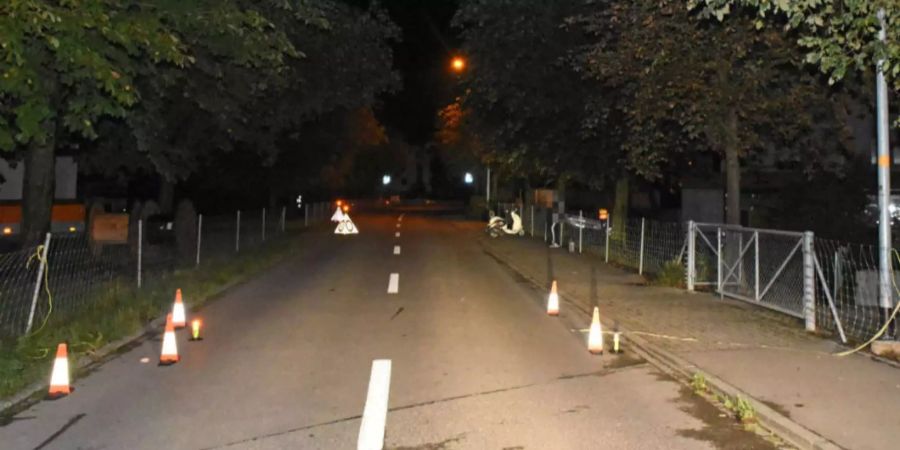 Die zerrissene, gelbe Schnur, die über die Strasse in Islikon TG gespannt war, ist noch an den Pfosten der Metallzäune befestigt. Polizei-Hütchen markieren die Stelle, an der die Rollerfahrerin verunfallte.