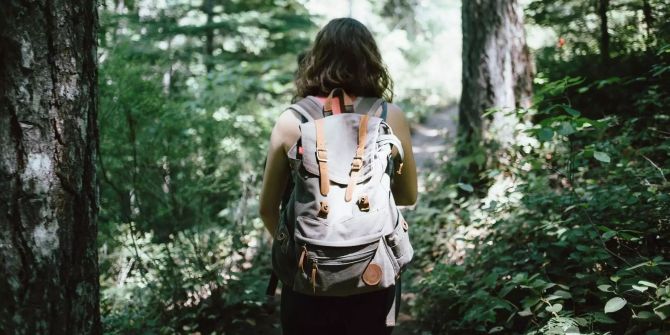 Ein Rucksacktouristin wandert auf einem Waldweg.