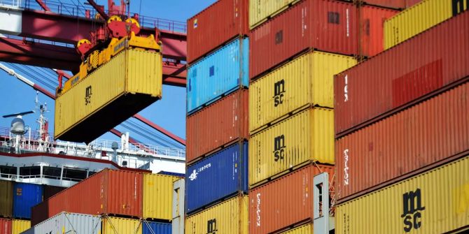 Ein Container wird im Hafen auf ein Containerschiff geladen.