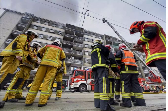 Feuerwehrleute stehen vor rauchendem Gebäude - Keystone Feuerwehrleute stehen vor rauchendem Gebäude - Keystone