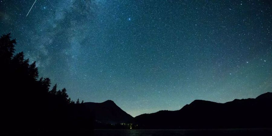 Eine Meteor leuchtet neben der Milchstrasse am Himmel über dem Walchensee (D).