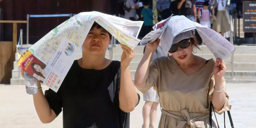 Frauen schützen sich in Südkorea mit einer Tageszeitung vor den Sonnenstrahlen.