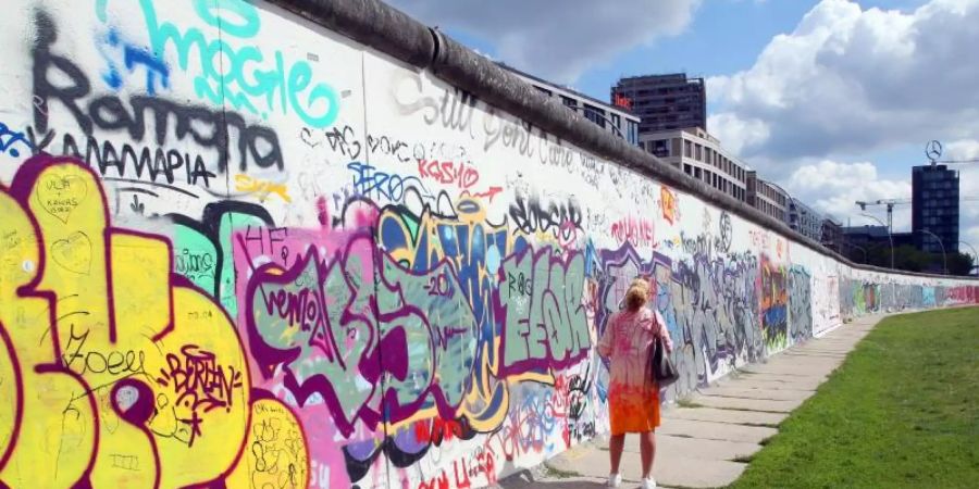 Eine Frau betrachtet an der East Side Galery im Bezirk Friedrichshain-Kreuzberg die bemalten Betonsegmente der Berliner Mauer. Foto: Wolfgang Kumm/dpa