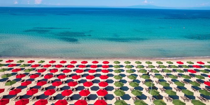 Sonnenschirme in rot und grün am Strand und Meer.