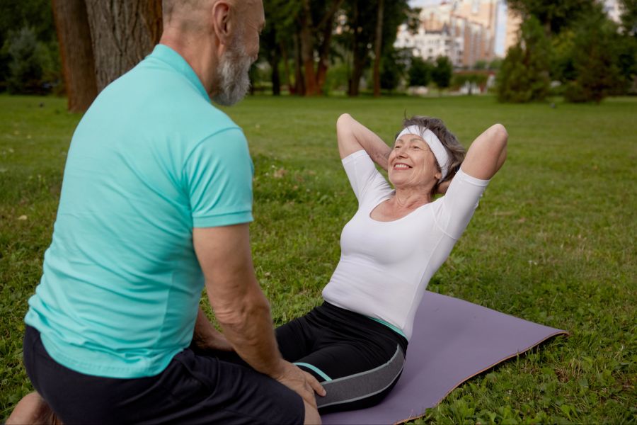 Ältere Frau macht Crunches, älterer Mann hilft der Frau beim Training