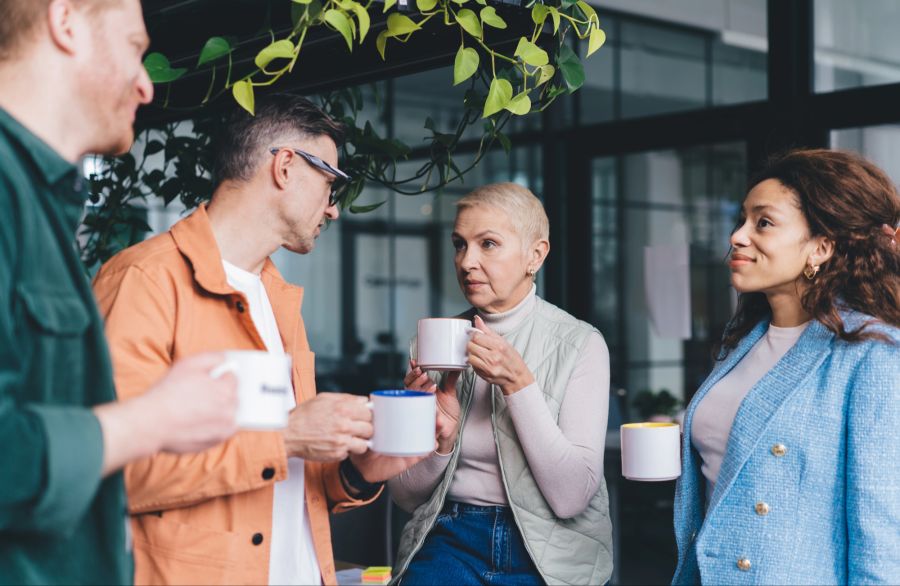 Zwei Männer und zwei Frauen trinken Kaffee am Arbeitsplatz und unterhalten sich