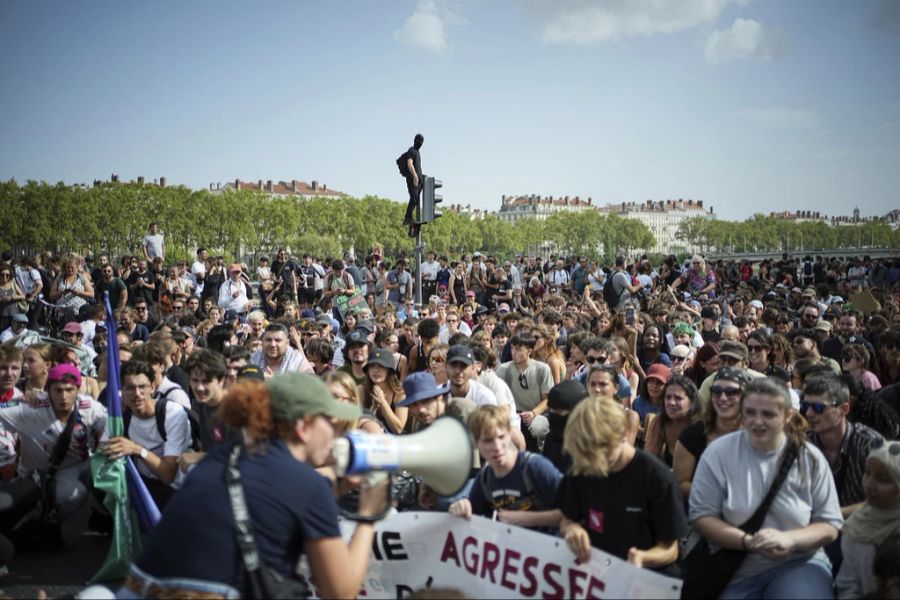 Der Platz in Lyon ist gefüllt mit Protestierenden. Ein Vermummter ist auf eine Ampel geklettert.