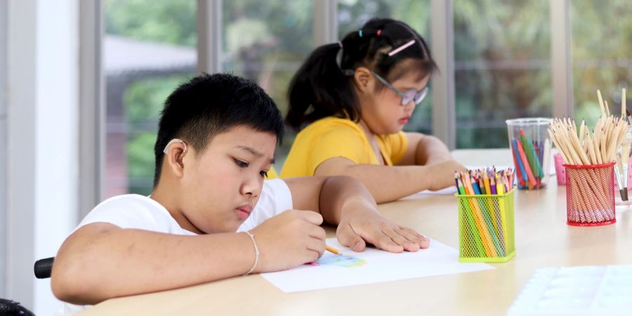 Behinderte Kinder sitzen am Tisch und malen