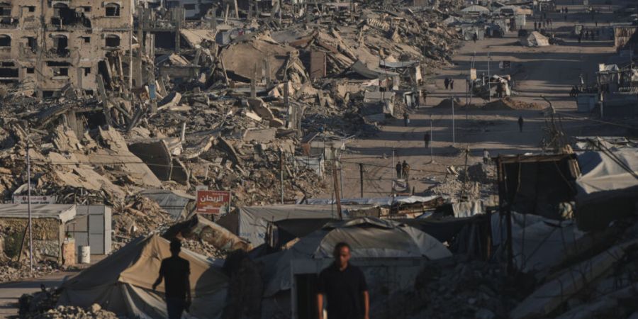 ARCHIV - Palästinenser gehen in Jabalia im Gazastreifen eine Straße entlang, die von Gebäuden gesäumt ist, die bei israelischen Militärangriffen während des Krieges zwischen Israe...