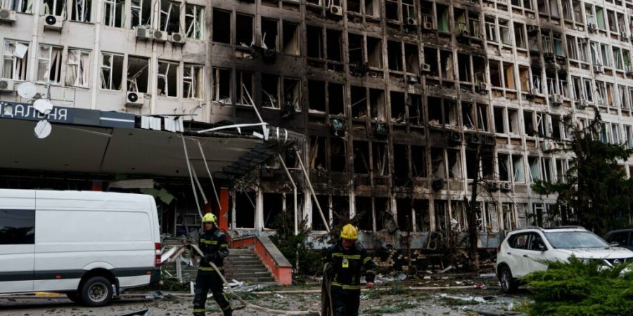 Rettungskräfte rollen vor einem Bürogebäude, das durch einen russischen Drohnenangriff beschädigt wurde, Feuerwehrschläuche auf. Foto: Evgeniy Maloletka/AP/dpa