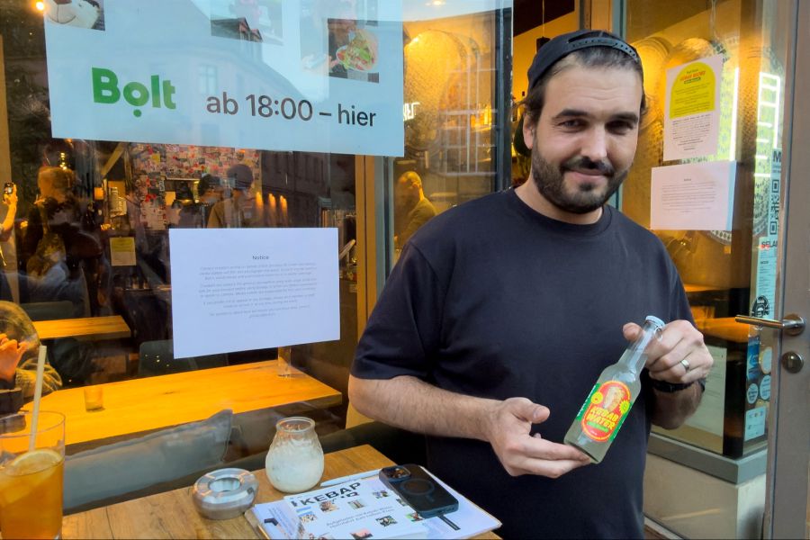 Beizer Deniz Buchholz hält eine Flasche «Kebab Water» vor seinem Dönerladen «Kebap with Attitude» in den Händen.