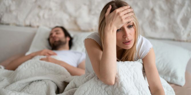 Genervte, nachdenkliche Frau, im Hintergrund schläft ein Mann