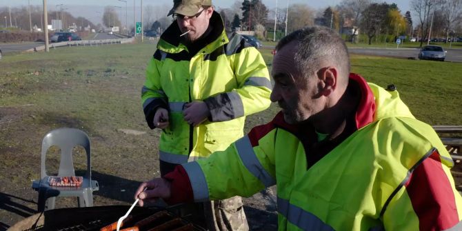 Demonstranten mit gelben Westen grillen an einer Verkehrsinsel Würstchen.