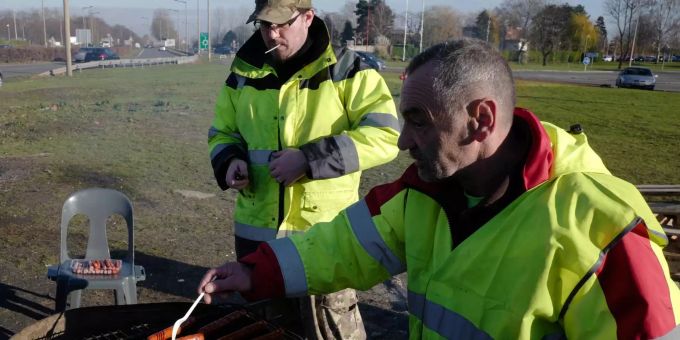 Die Gelbwesten-Demonstranten sollen vorerst besser zu Hause bleiben – Würstchen grillen ist auch ok. Demonstranten mit gelben Westen grillen an einer Verkehrsinsel Würstchen.