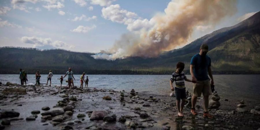 Eine Familie läuft im Yosemite-Nationalpark an einem See entlang. Im Hintergrund wütet ein Waldbrand.