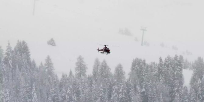 Ein Helikopter fliegt über verschneite Bäume.