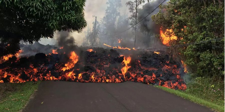 Ein Lavastrom wälzt sich über eine Strasse. Der Vulkanausbruch auf Hawaii hat erste Zerstörungen verursacht. Mindestens 26 Häuser im Wohngebiet Leilani Estates östlich des Kilauea auf Hawaiis grösster Insel Big Island seien von Lavaströmen vernichtet worden, teilte die Zivilschutzbehörde mit.