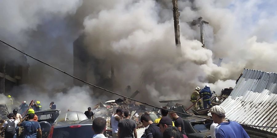 Zivilisten und Feuerwehrleute befinden sich an der Unfallstelle während Rauch aufsteigt. Nach einer schweren Explosion in einem Einkaufszentrum sind nach offiziellen Angaben einige Menschen verletzt oder tot. Foto: Daniel Bolshakov/AP/dpa