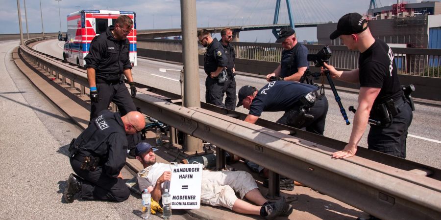 Polizisten versuchen auf der Köhlbrandbrücke zwei mit einem Eisenrohr miteinander verbundene Klimaaktivisten zu lösen.