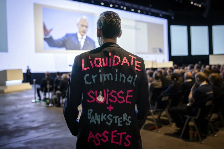 Ein Mann trägt einen Anzug mit der Aufschrift «Liquidate Criminal Suisse + Banksters Assets».