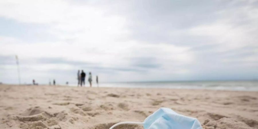 Ein gebrauchter Mundschutz mit Resten von Lippenstift liegt am Strand vor der Strandpromenade von Westerland auf Sylt. Foto: Christian Charisius/dpa